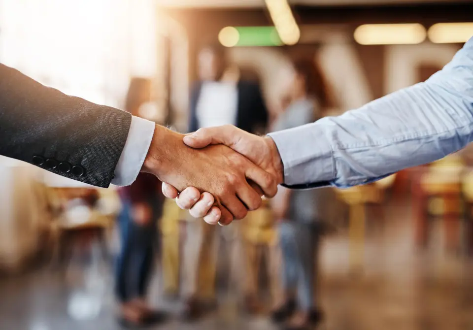 Handshake of business men with co-workers in the background.